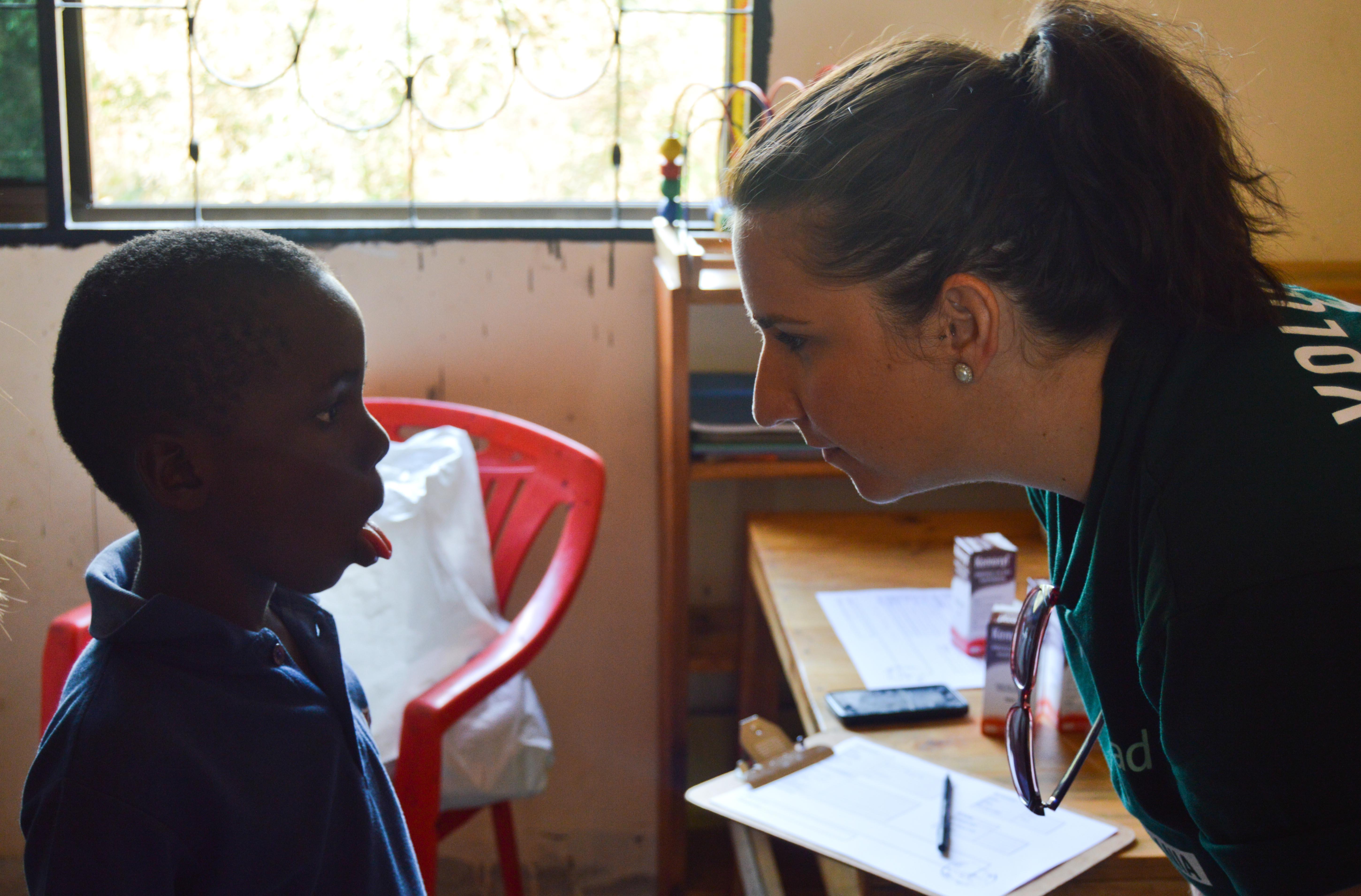 Female Dentistry intern examines a young boy's throat at a dental clinic as part of her dentistry work experience in Tanzania. A young boy has his mouth and throat examined by a Projects Abroad Dentistry intern during an outreach in Tanzania.